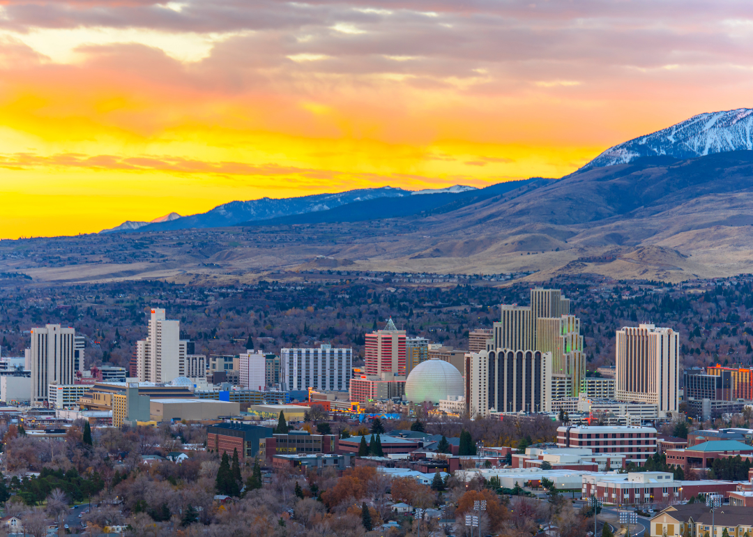An aerial view of downtown Reno with a bright orange sunset and mountains in the background.