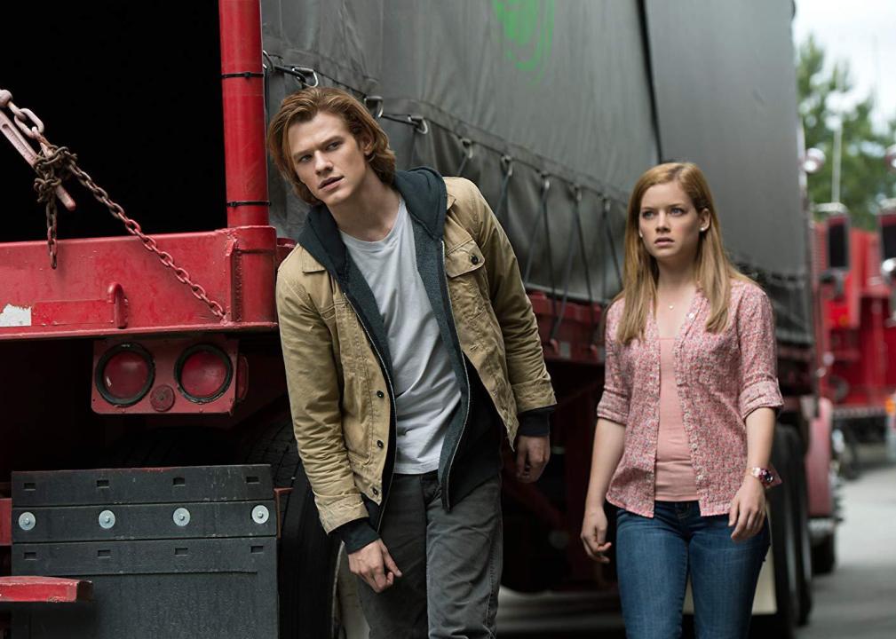 A young man and woman sneak alongside a truck.