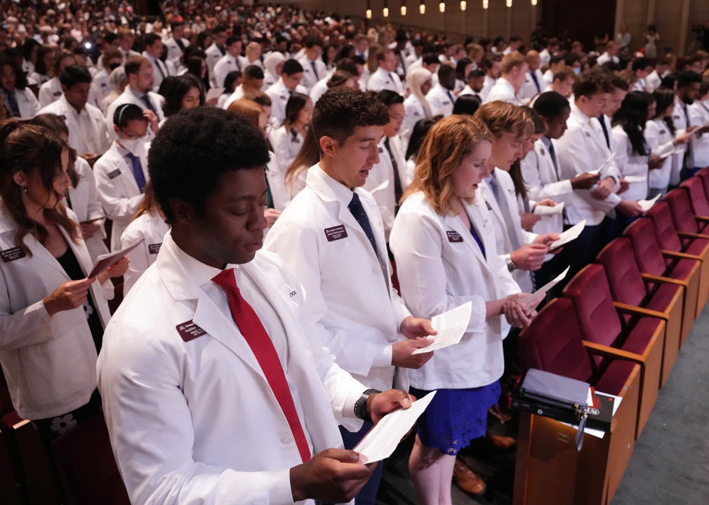 Medical students in white coats recite an oath for their White Coat Ceremony graduation in an auditorium.
