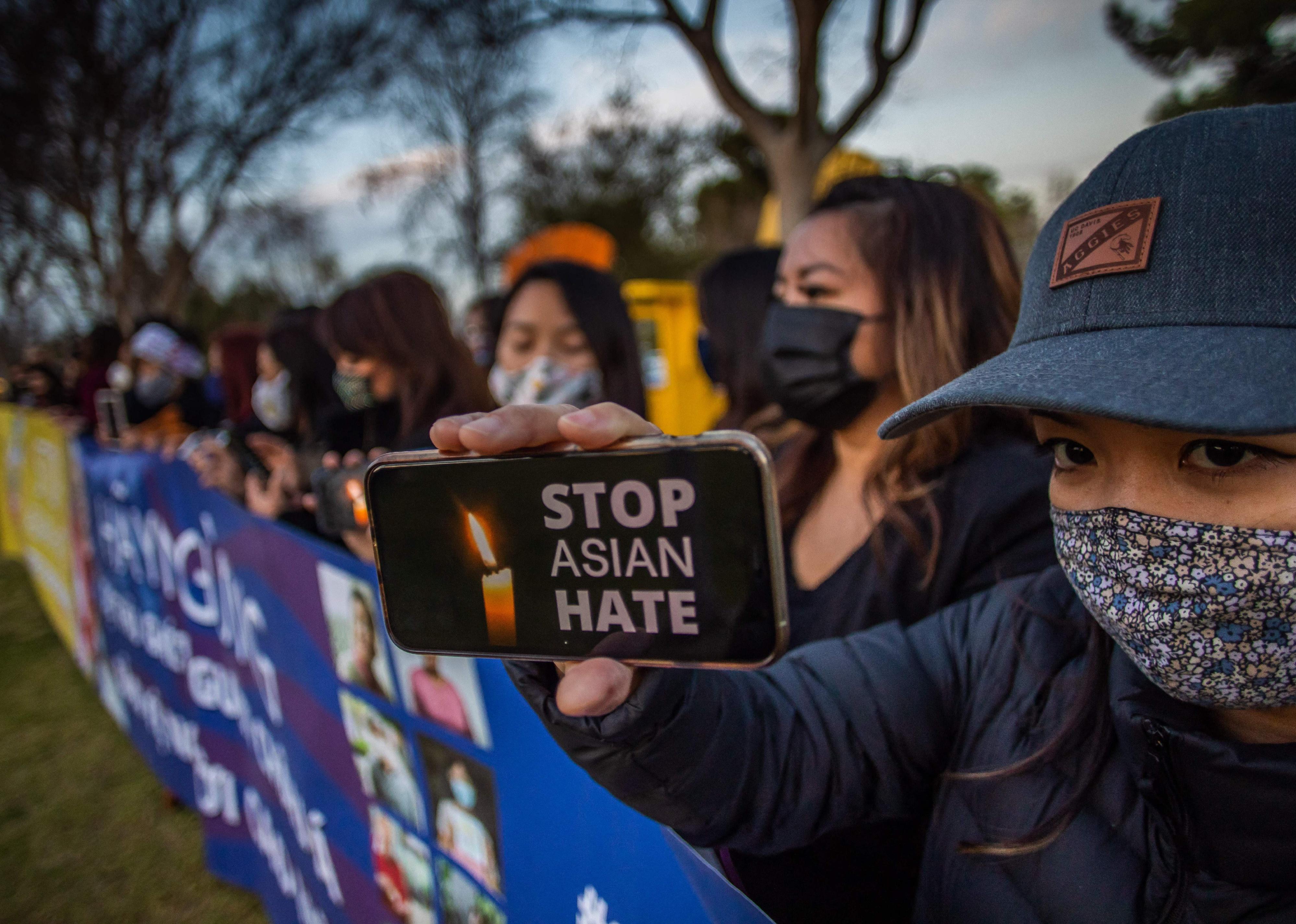 People wearing masks stand behind signs against Asian hate.