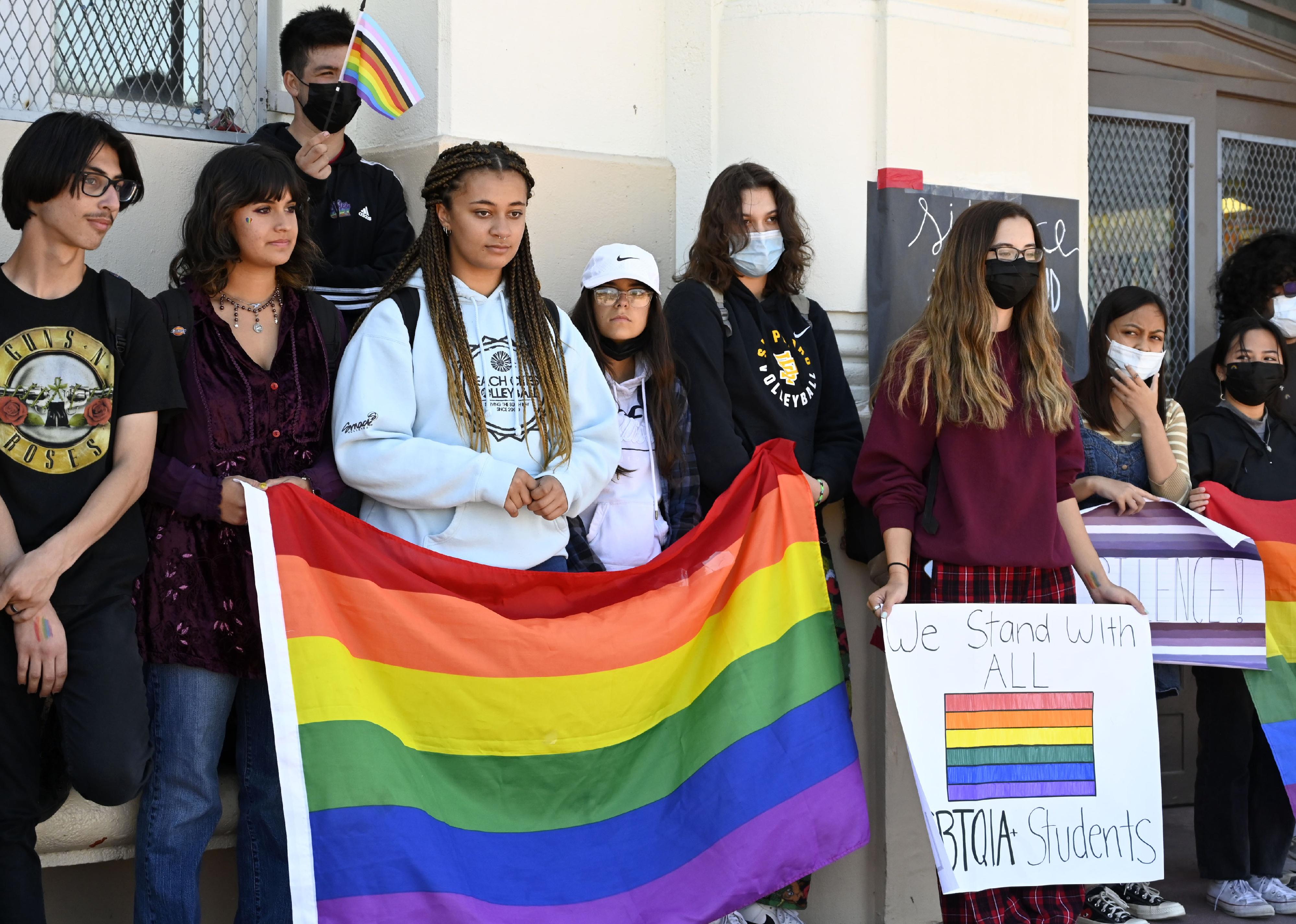 A group of high school students hold up signs and a pride flag.