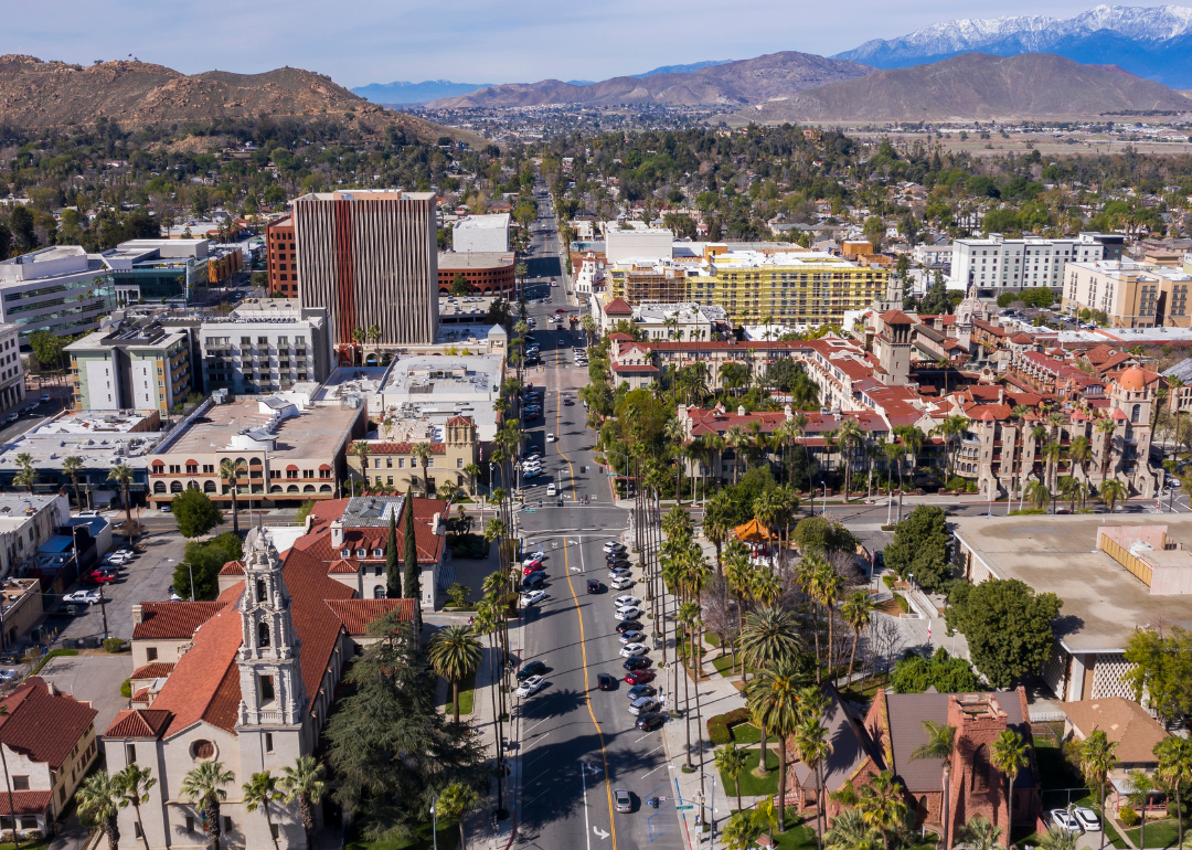 An aerial view of Riverside, California, downtown covered in palm trees and terra cotta rooftops with a mountainous backdrop