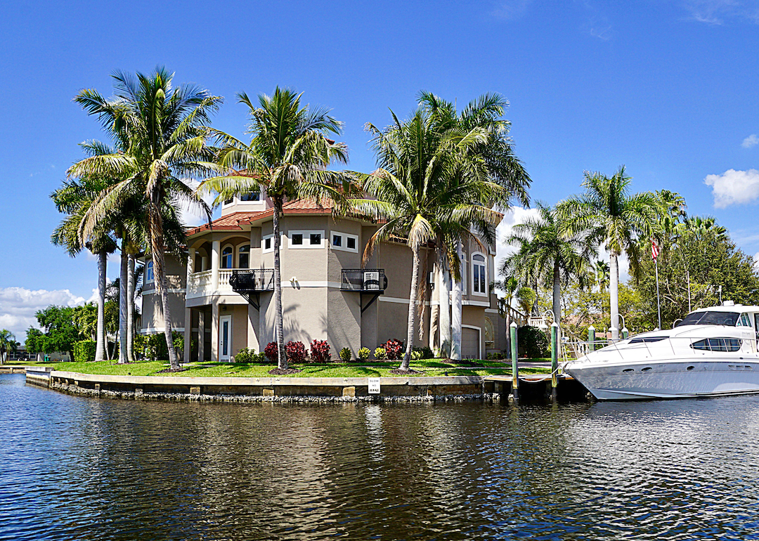 A large home with palm trees and a yacht on a waterway.