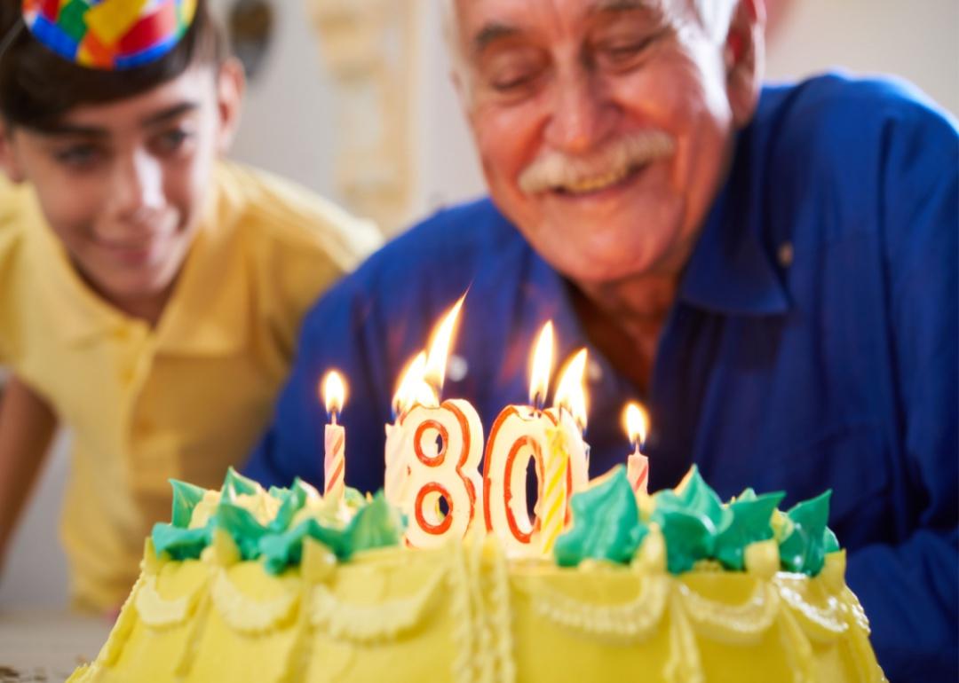 A man blowing out the candles on his 80th birthday cake with a child next to him.