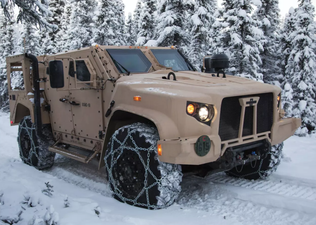 A tan tactical vehicle with snow chains on the wheels.