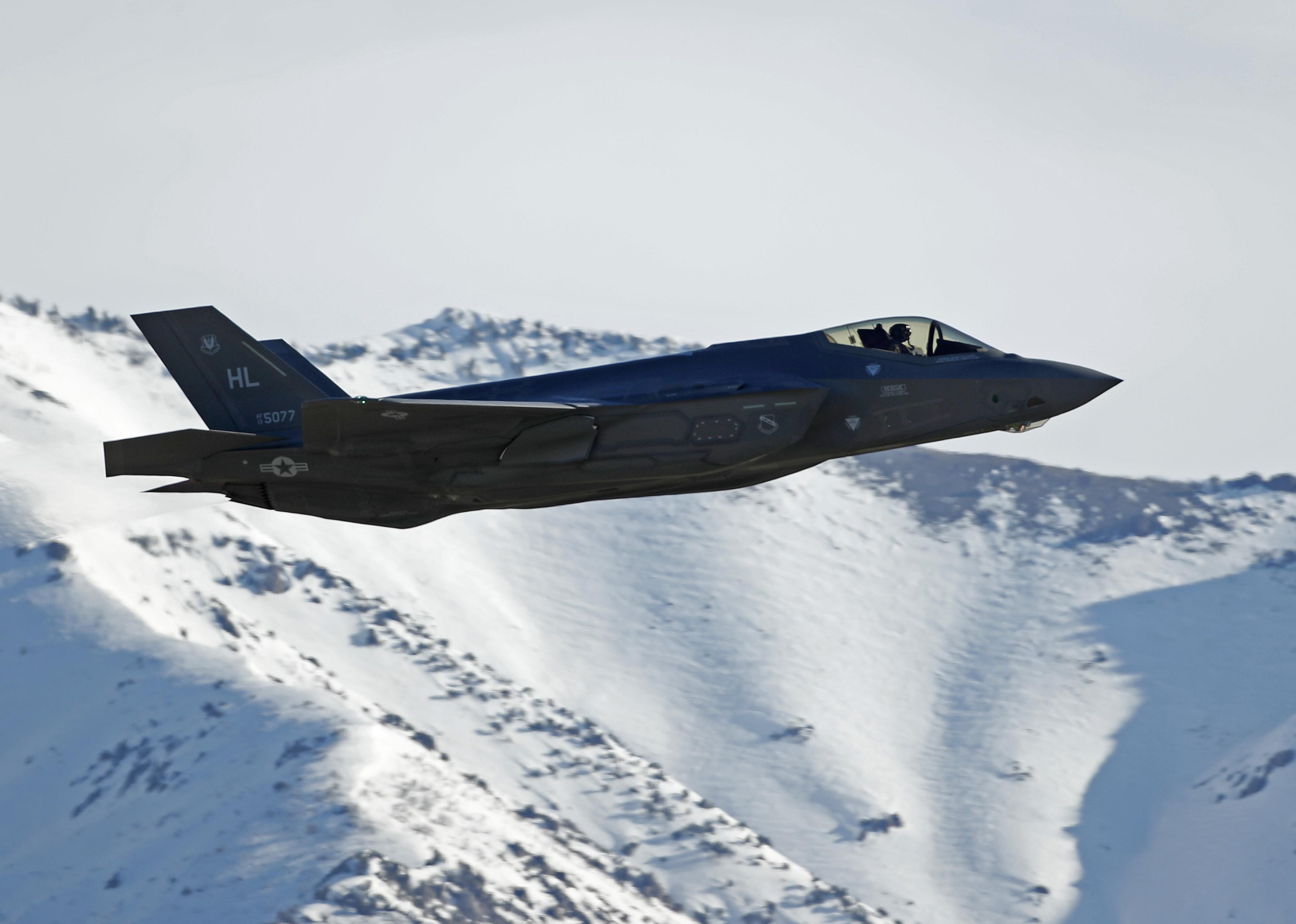 An F-35 jet flying over snowy mountains.
