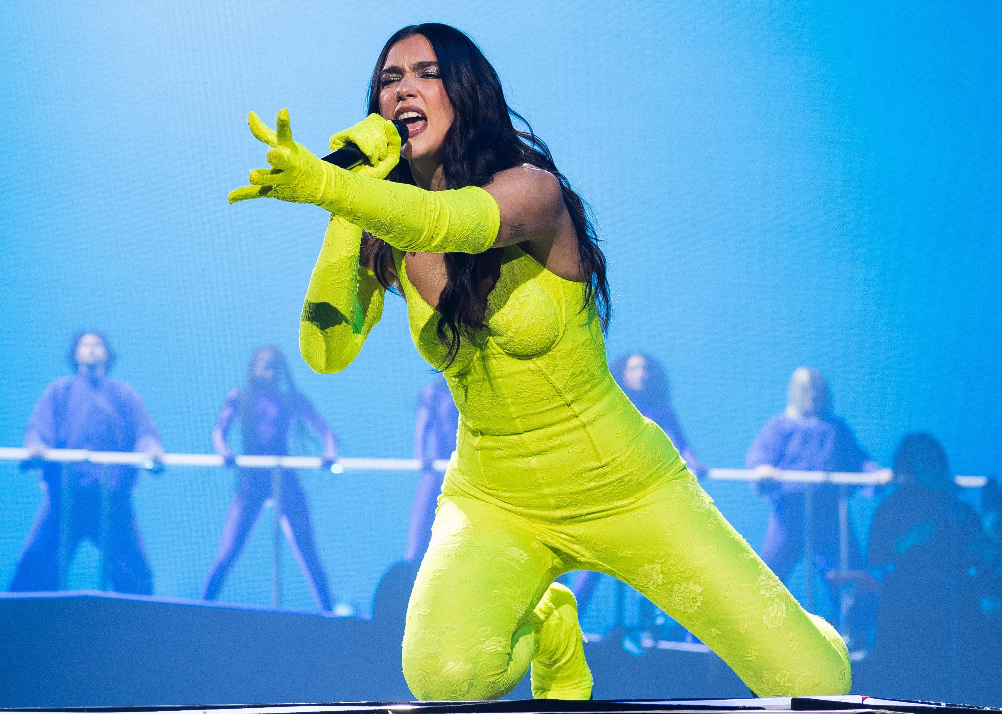 Dua Lipa performing onstage in a neon yellow green jumpsuit.