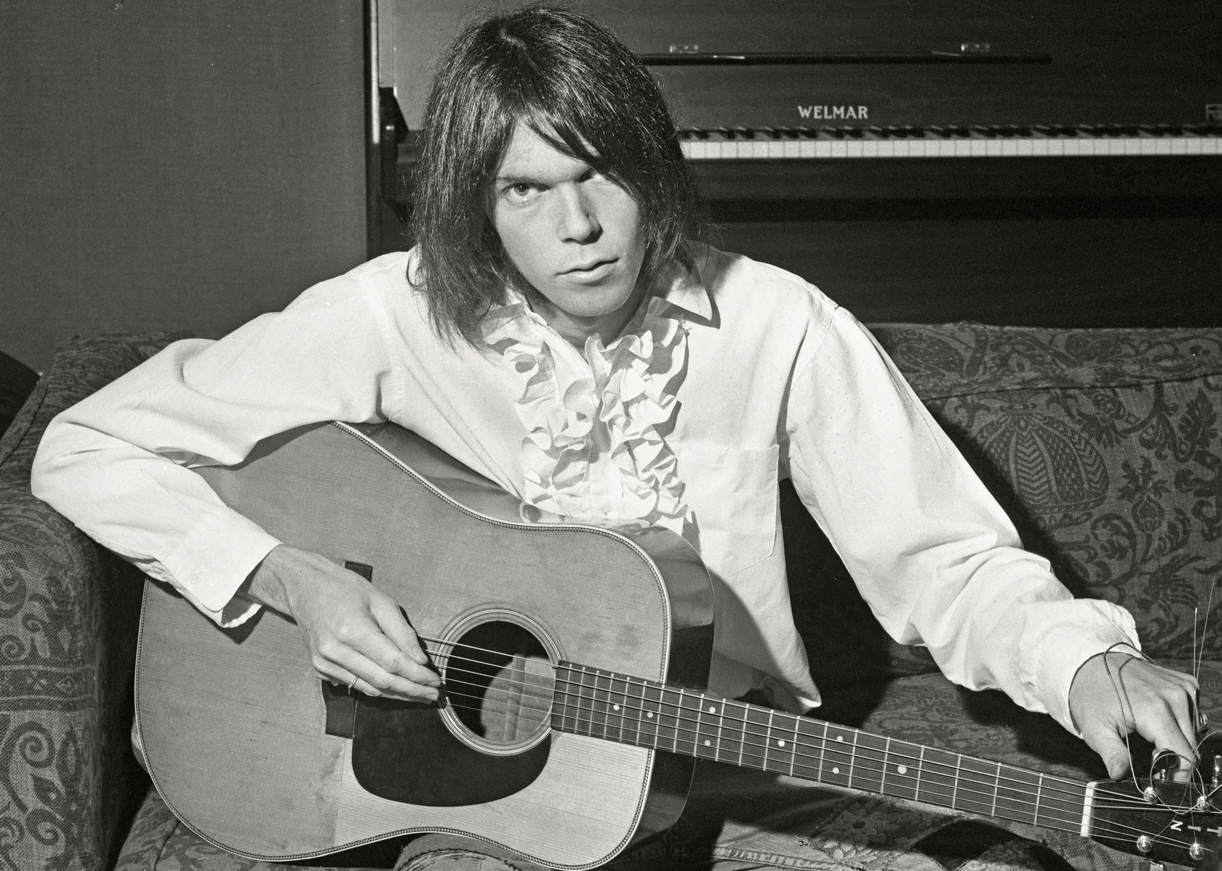 Neil Young holding a guitar on a couch.