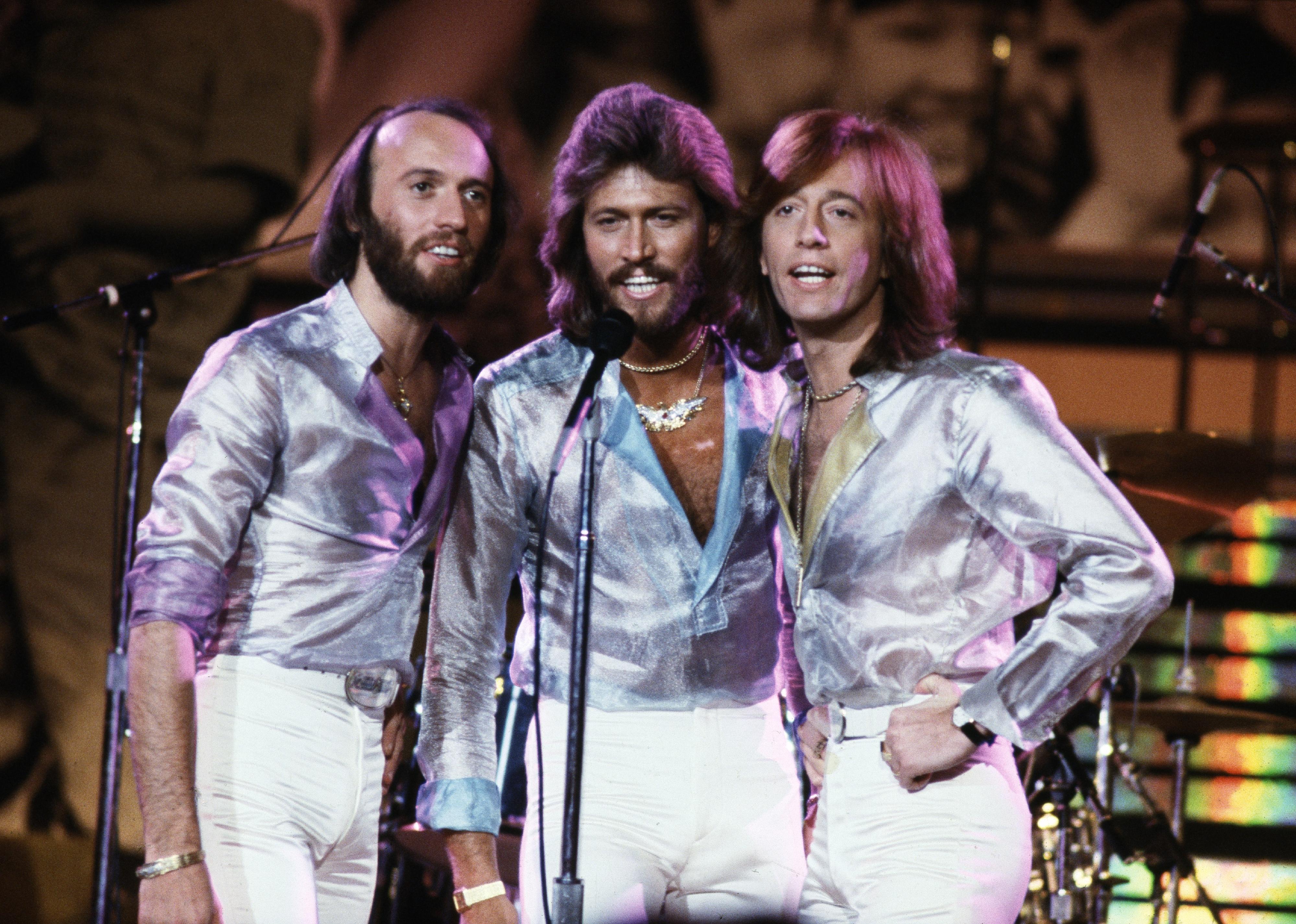 The Bee Gees wearing silver shirts onstage.