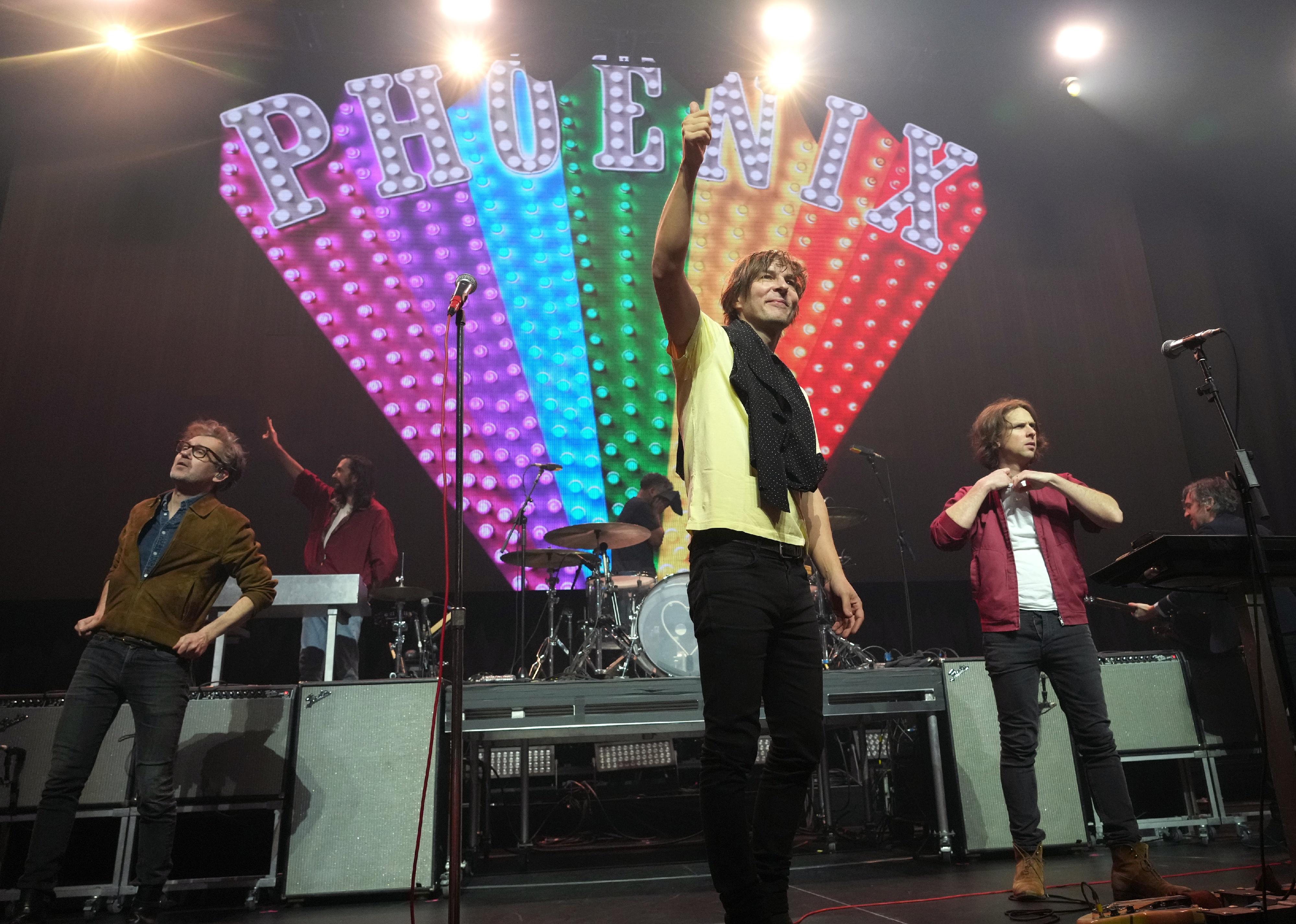 Phoenix performing onstage in front of a neon rainbow.