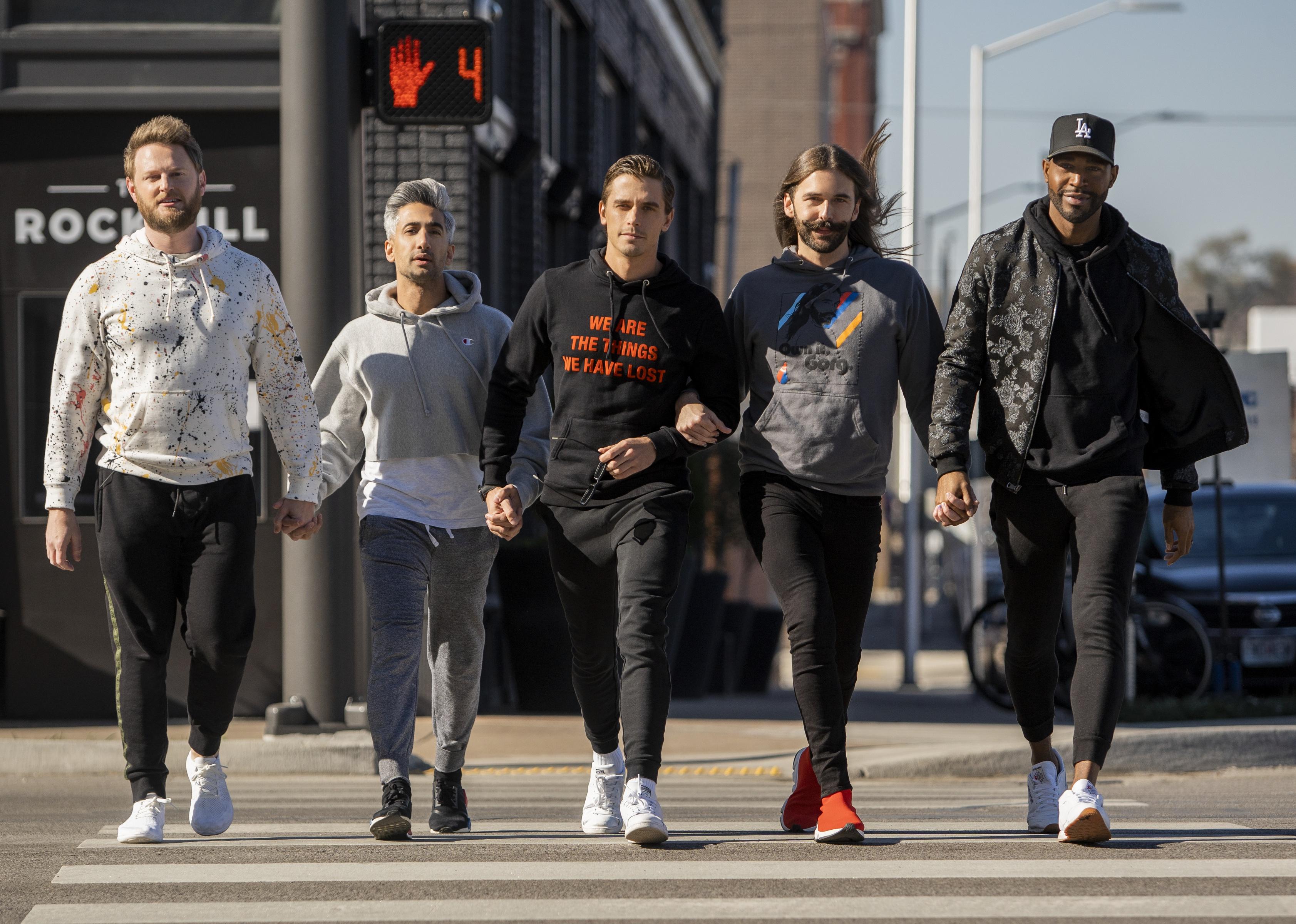 A group of guys holding hands walking across a street.