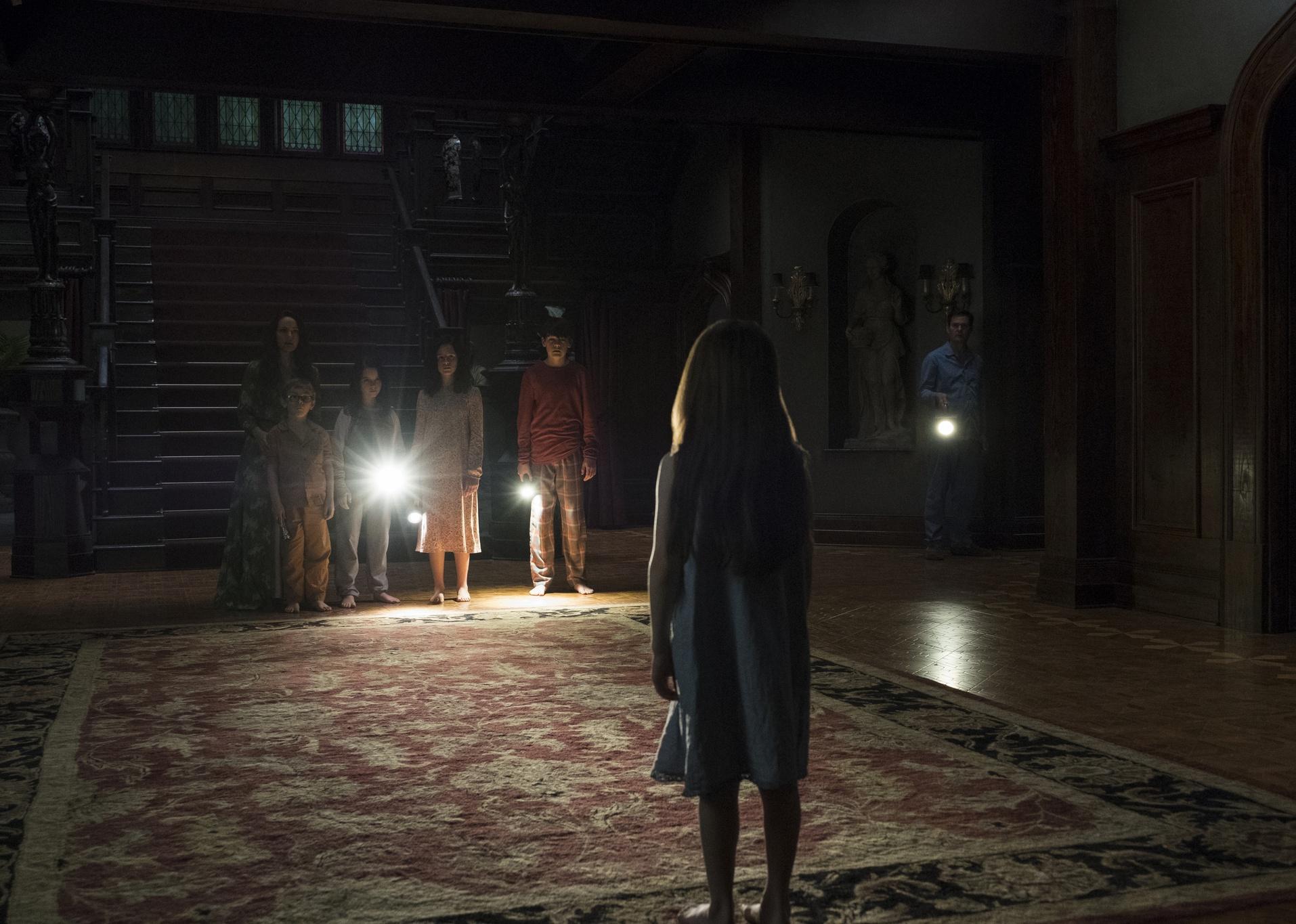 A family standing in a mansion in the dark with flashlights.
