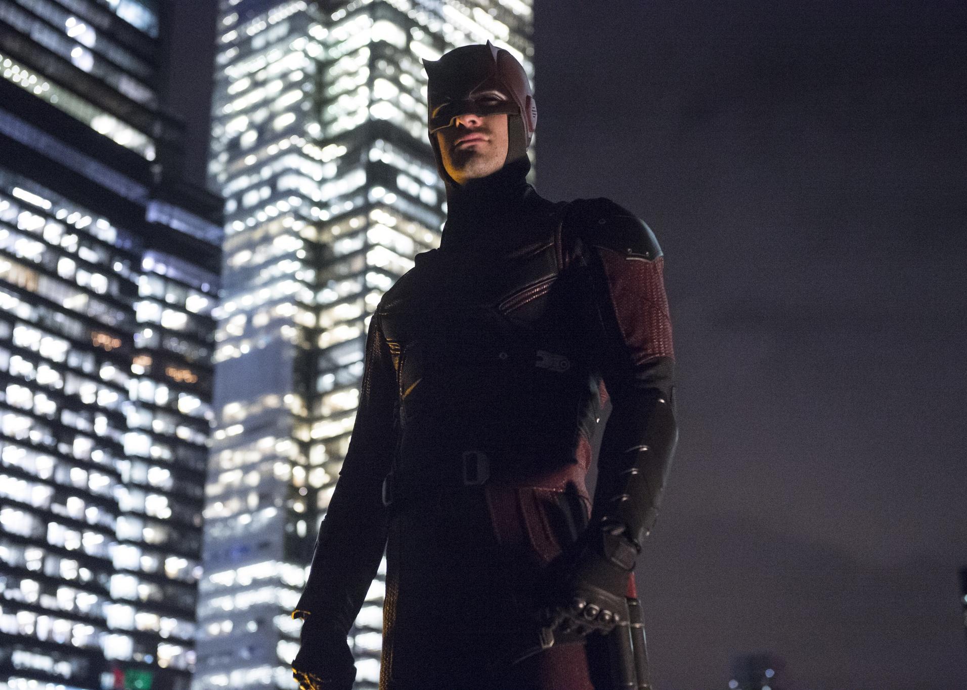 A superhero standing on top of a building in a red and black suit.