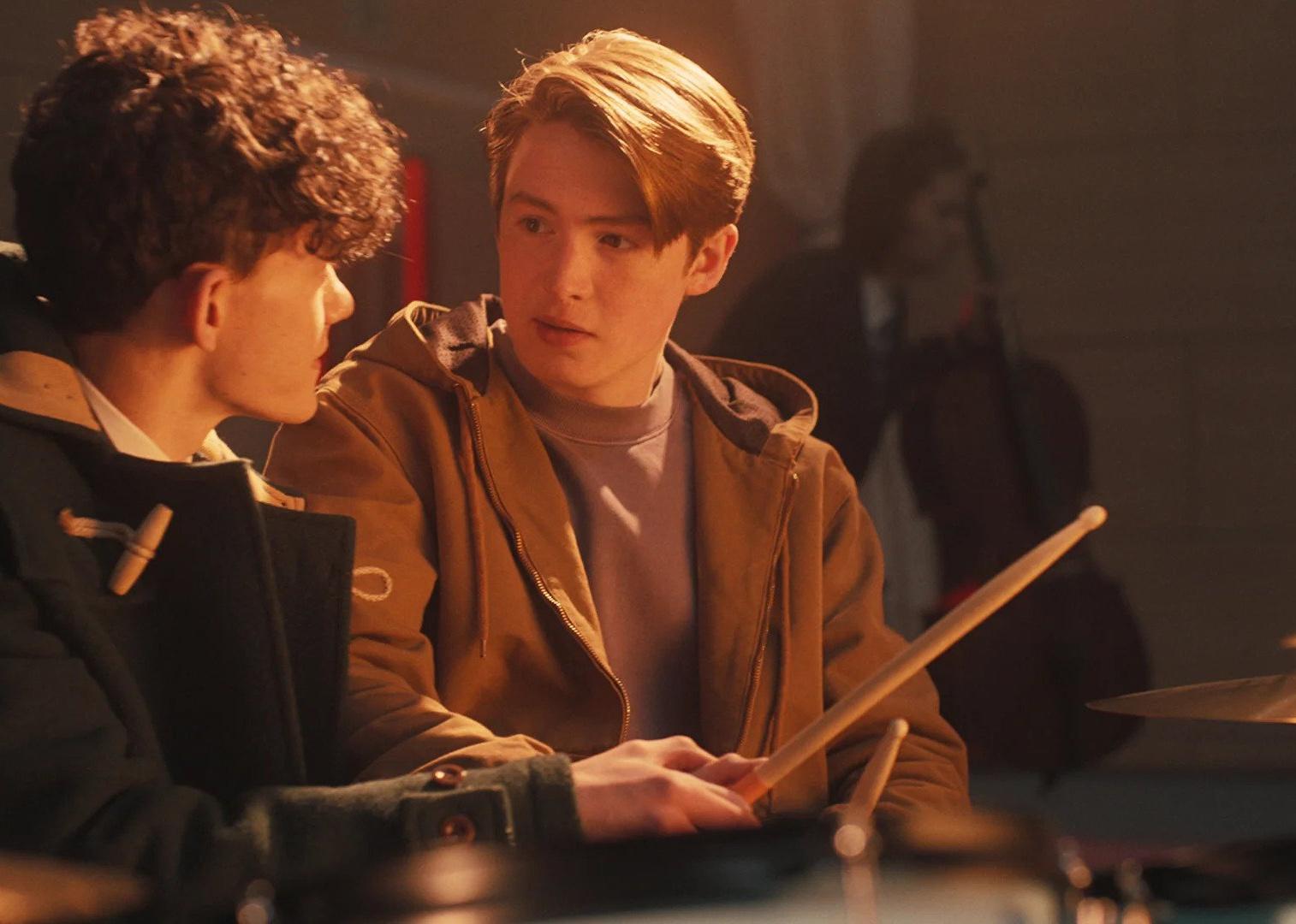 Two boys sitting at a drumset together.