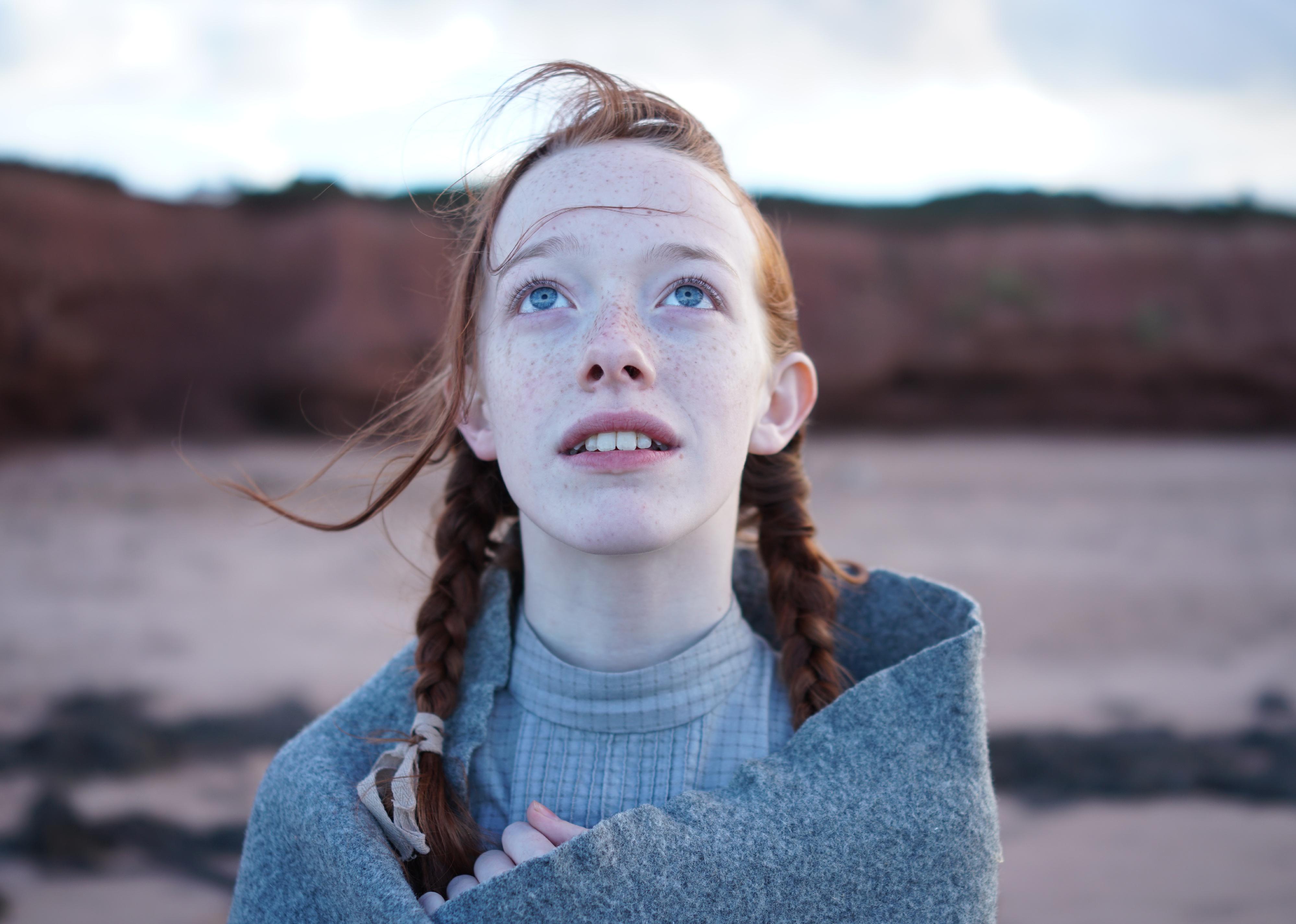 A girl, with red pigtail braids, wrapped in a blanket looking up at the sky.