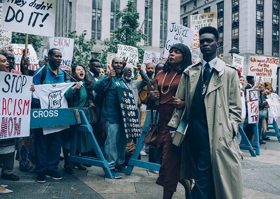 A black man and woman walking in front of protesters holding up equal rights signs.