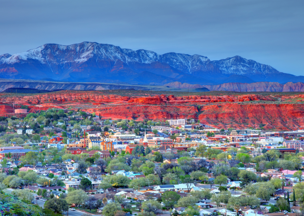 Aerial view of homes and buildings in St. George, Utah with orange mesa and snow-capped mountains in the background.