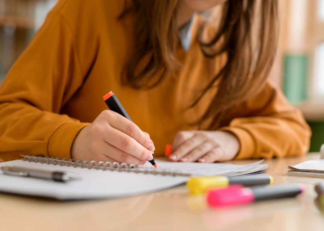 A young woman in an orange sweater takes notes in different colors.