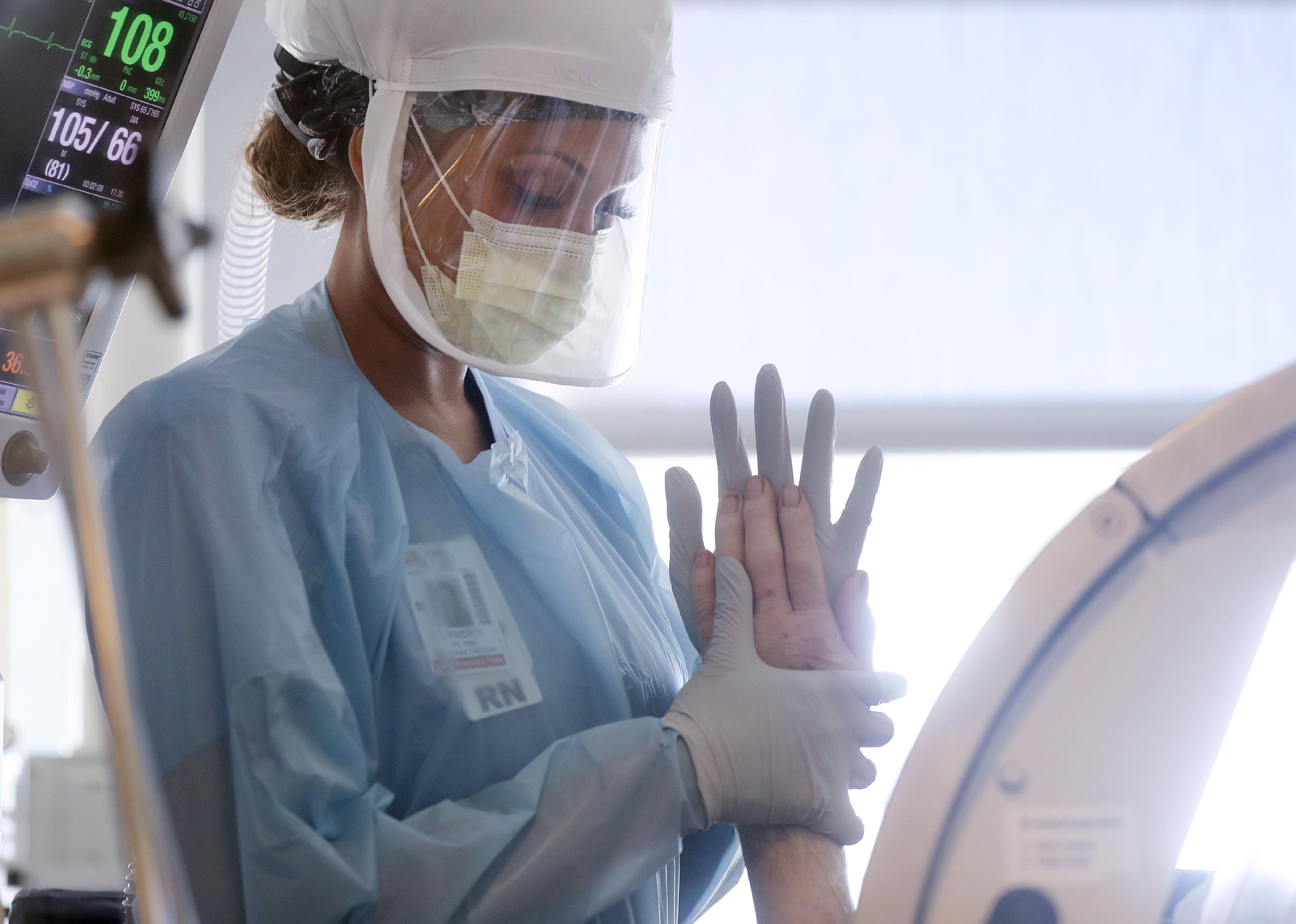A nurse in protective gear holds a patient's hand.