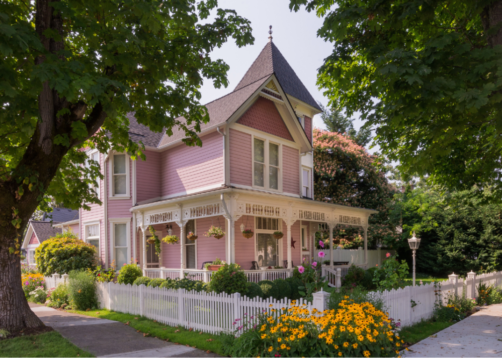 A pink Victorian house with yellow flowers in the front yard.