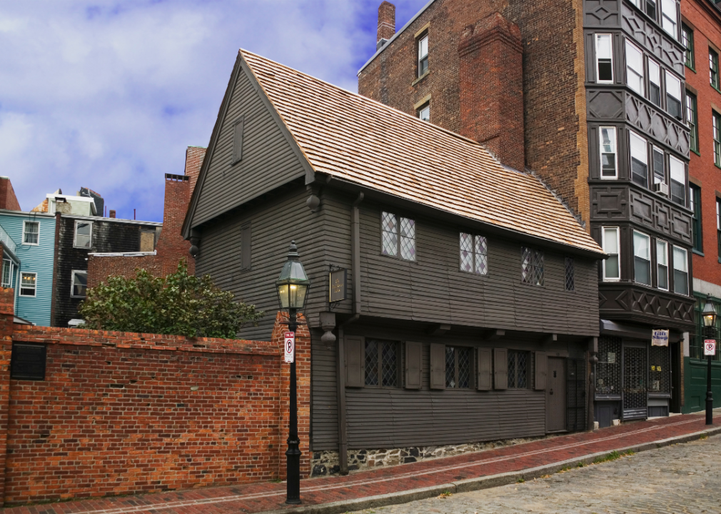 A brown house tucked away between brick buildings on a cobbled street.