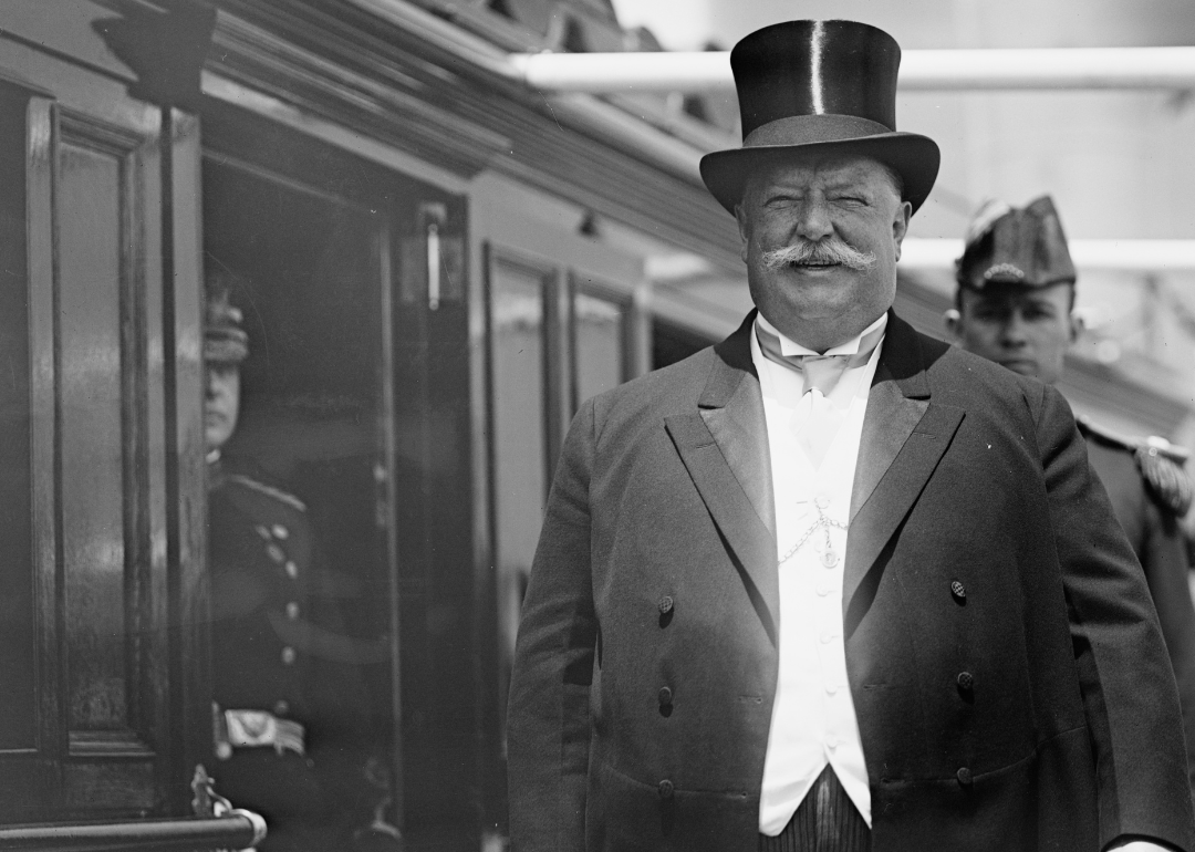 William Howard Taft in a suit and tophat next to a train.