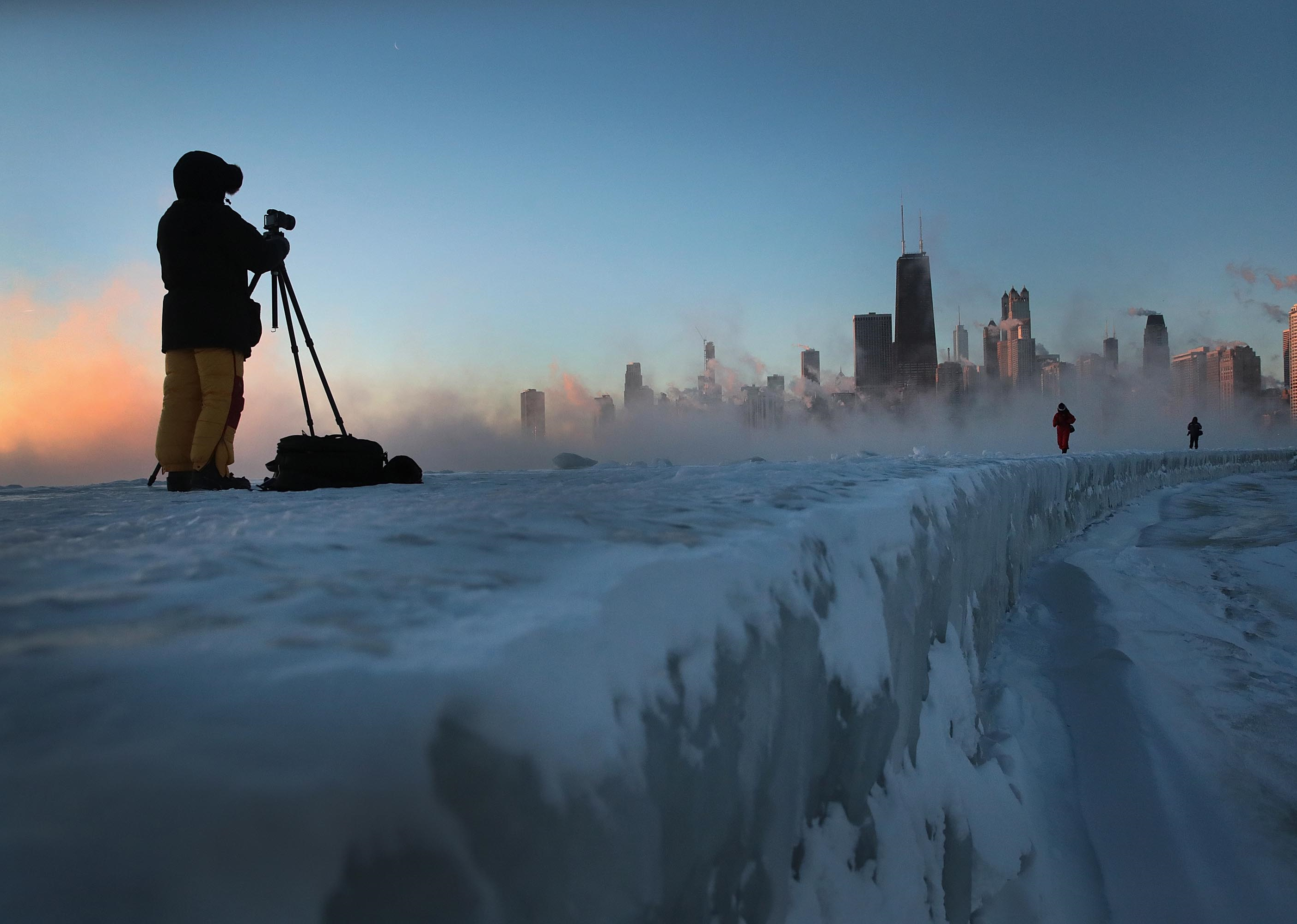 A photographer standing on the ice trying to take a picture of the sunrise over downtown Chicago.