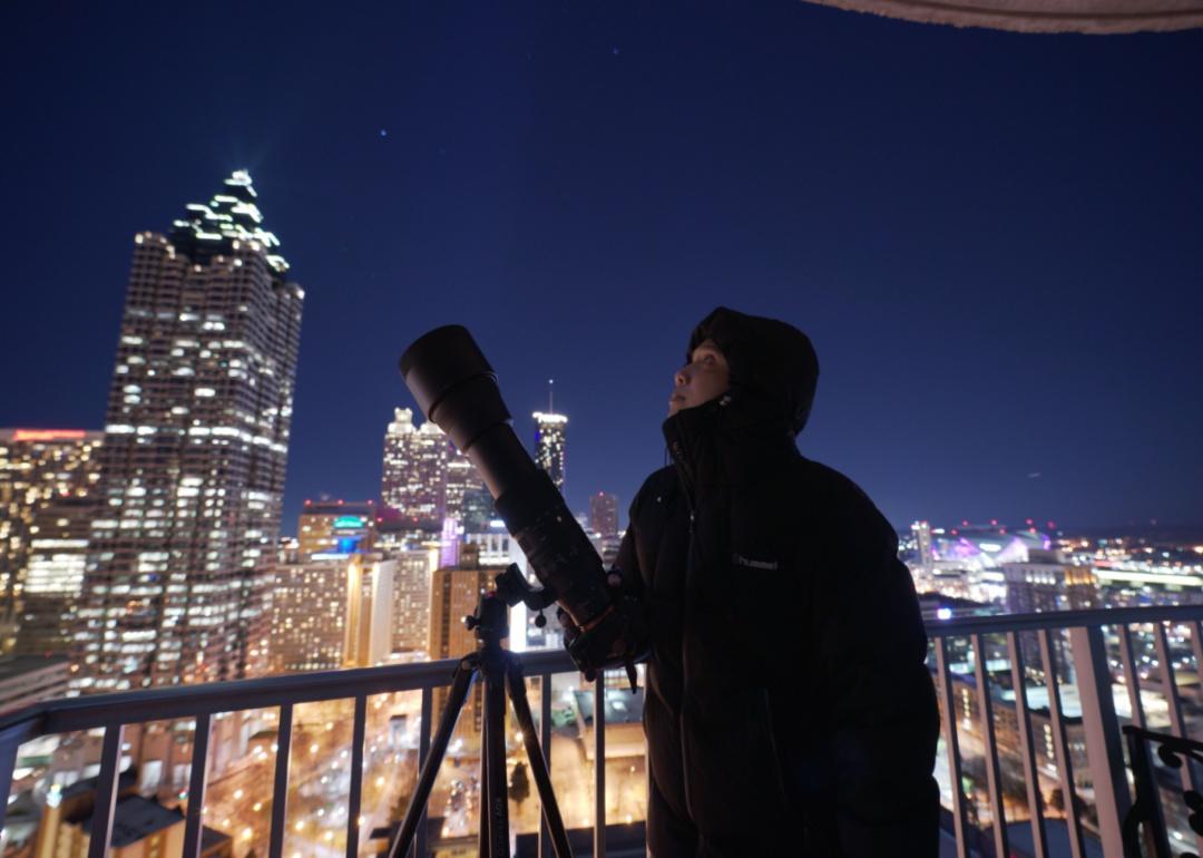 A person on a downtown balcony with a long-lens camera pointed at the sky.