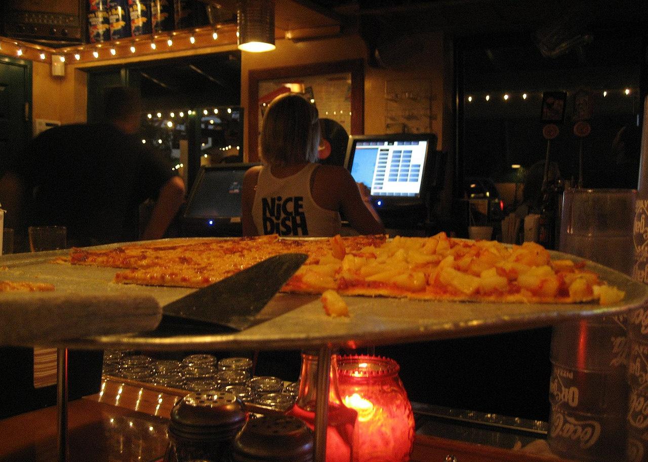 A half-eaten pizza on a table with a waitress in the background.