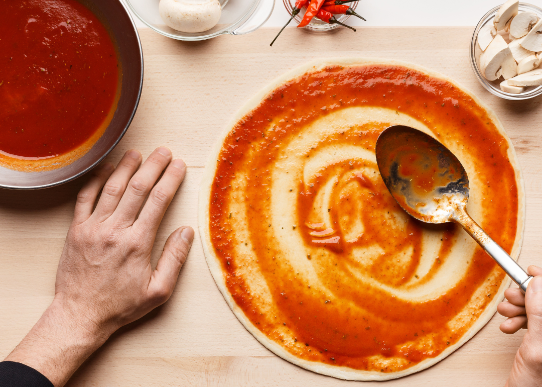 A person putting pizza sauce on a pizza crust.