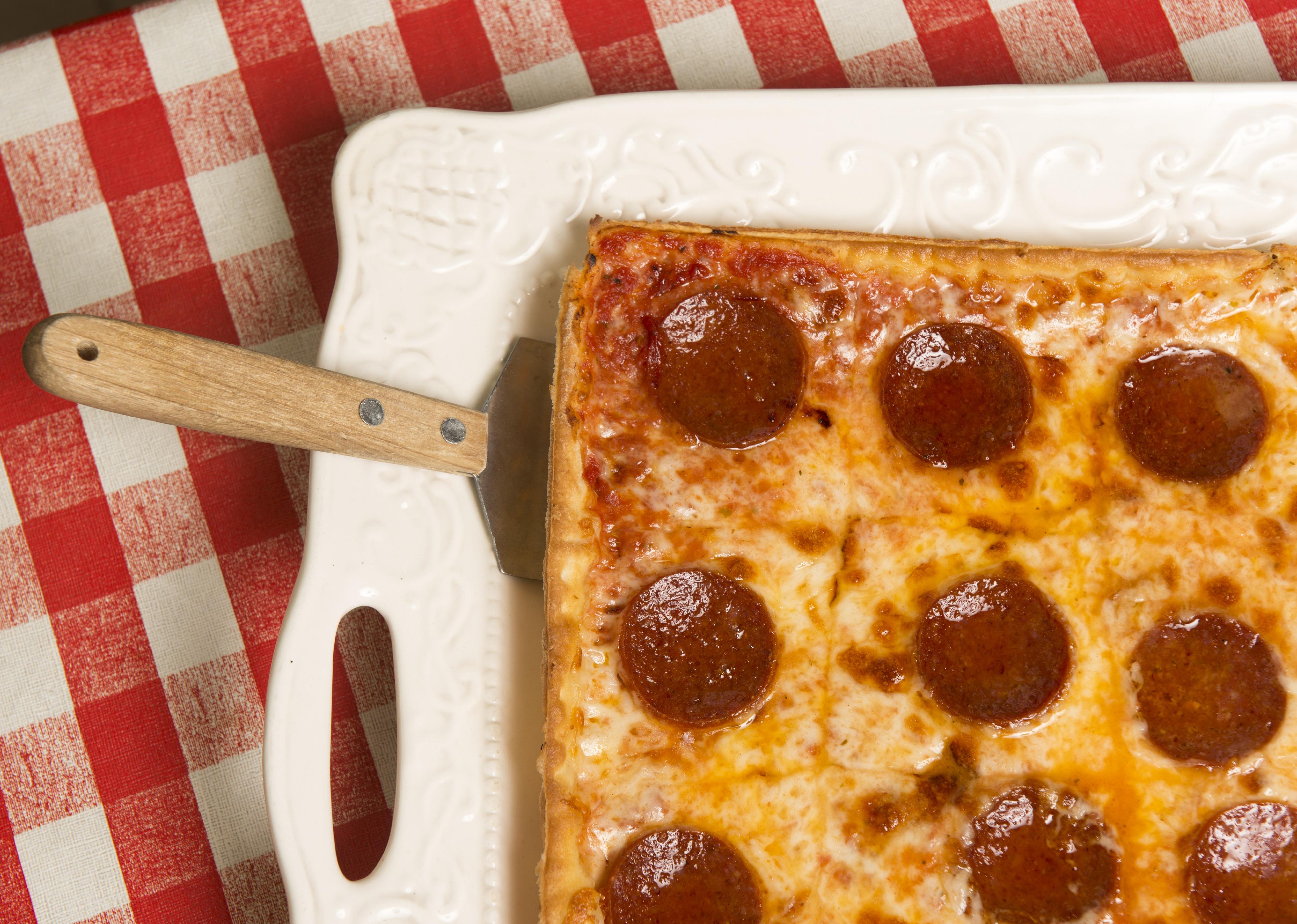 A rectangular pepperoni pizza on a red checkered table.