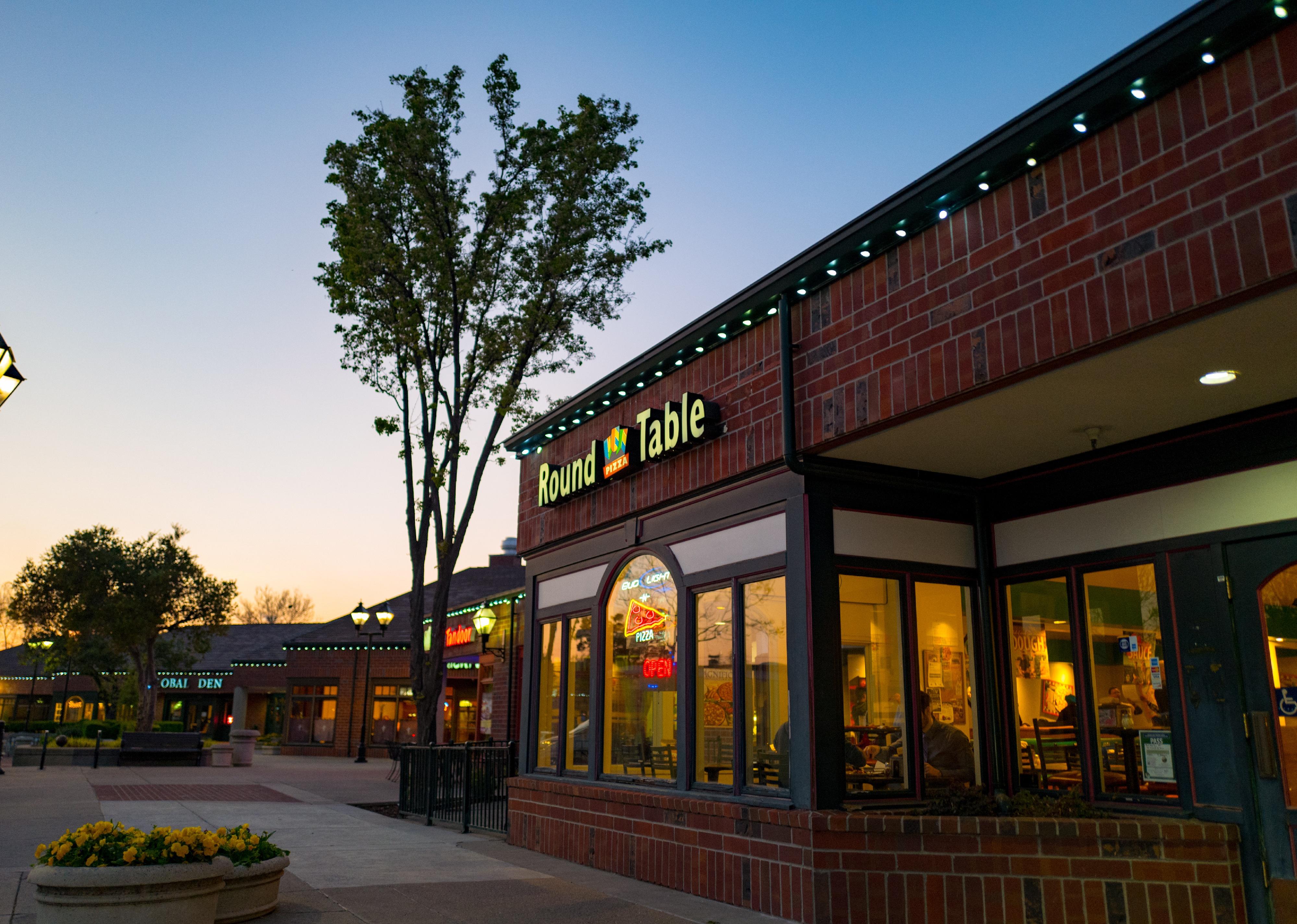 The exterior of a Round Table Pizza restaurant in a brick shopping center.