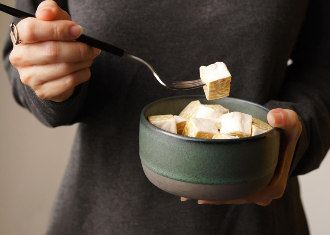 A person holding a fork of Tempeh over a bowl.