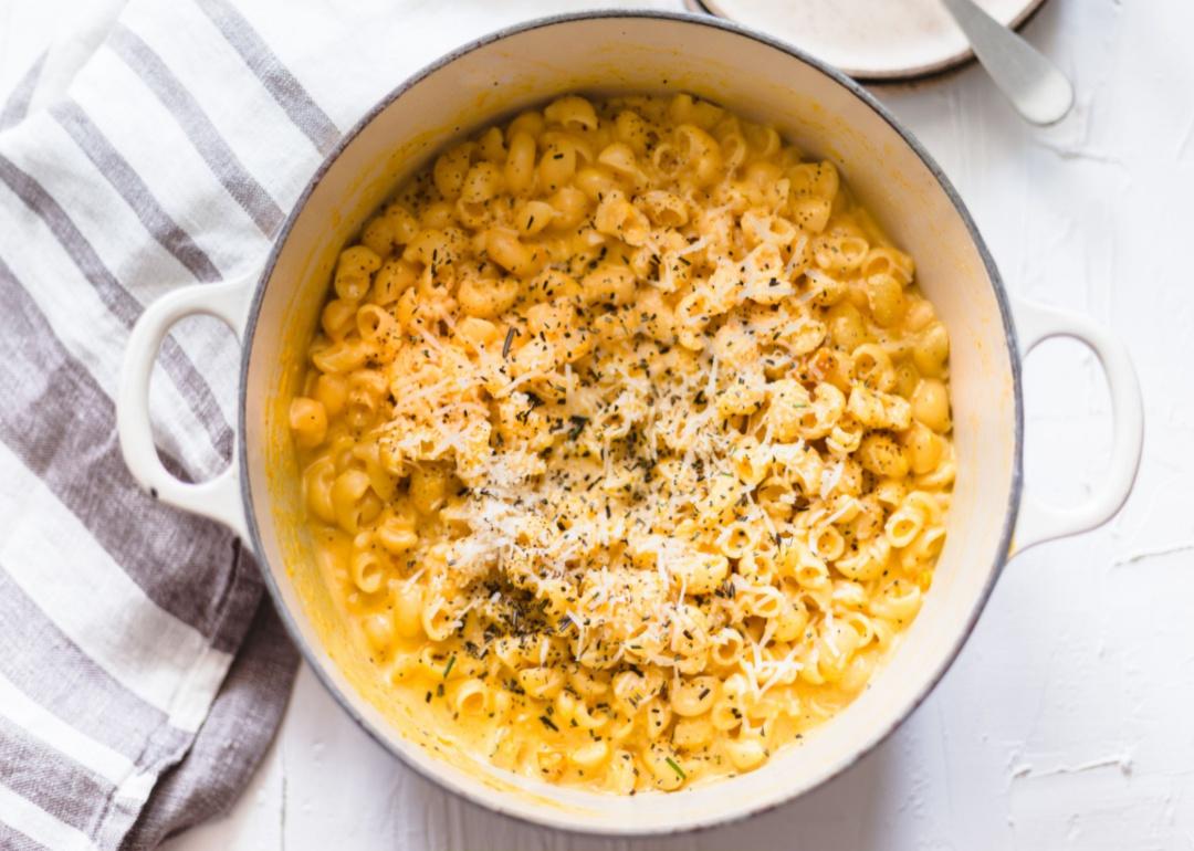 A white dutch oven dish of baked mac and cheese with a gray and white towel.