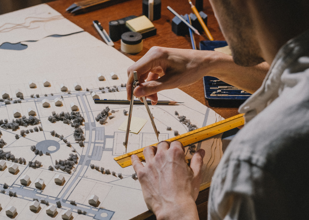 A person holding a protractor and working on an architectural model.