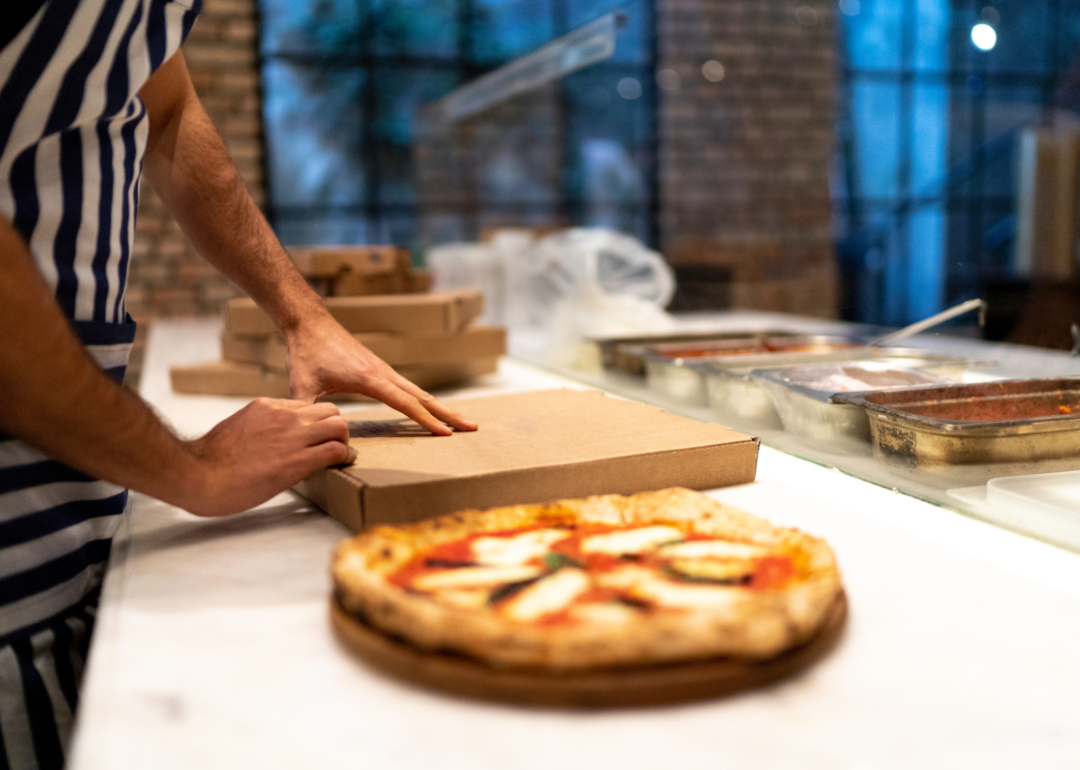 A man in a black and white striped apron preparing a pizza to go.