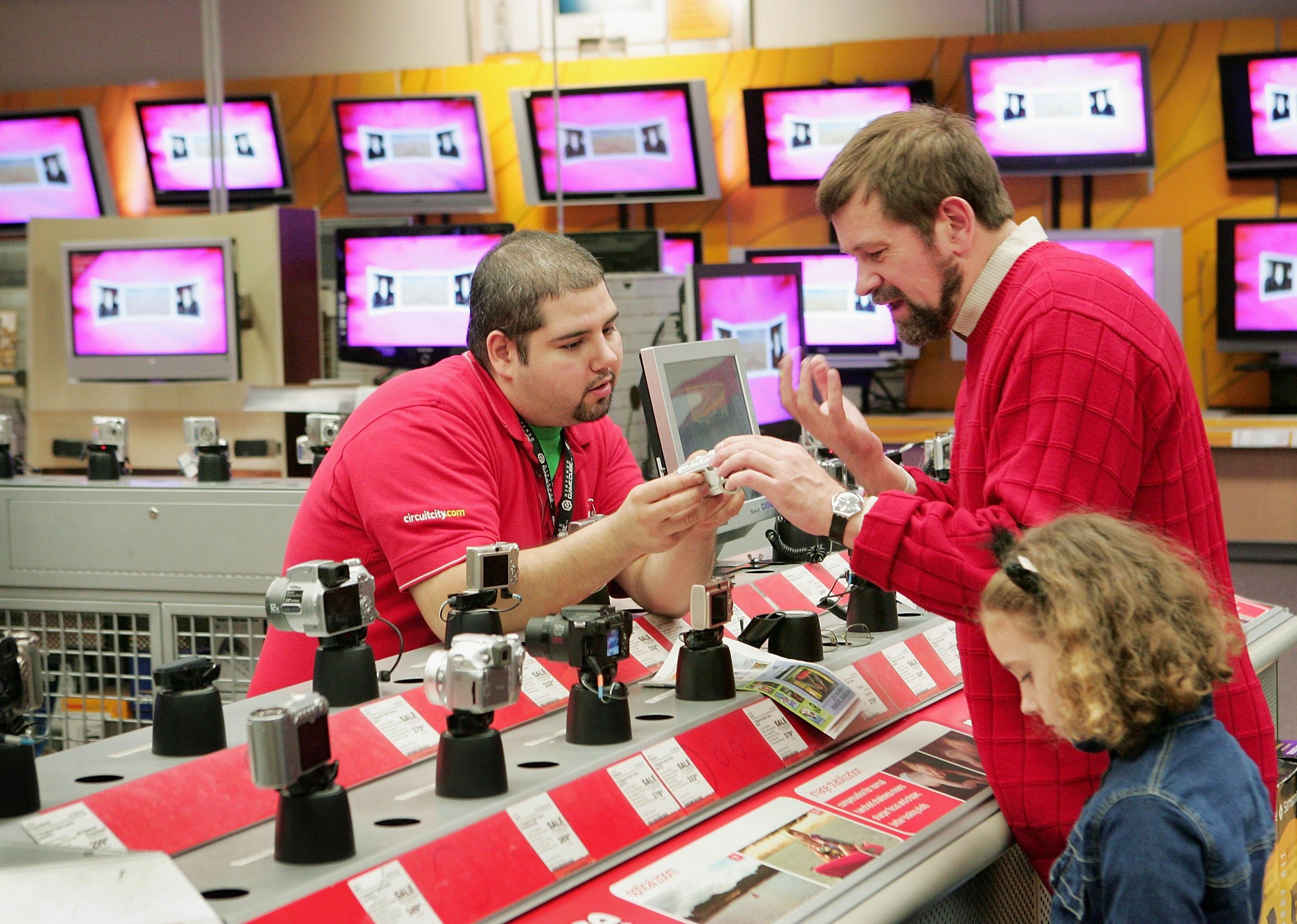A Circuit City employee demonstrates a camera for a man and a little girl.