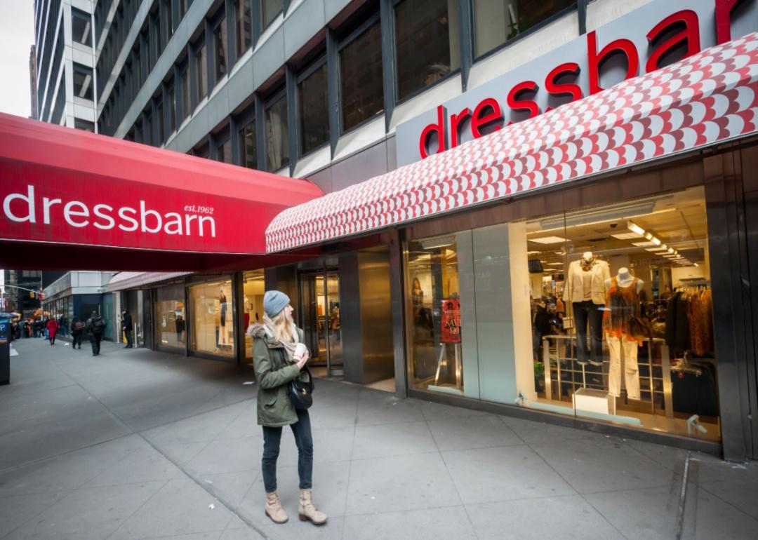 A woman walking in front of a Dressbarn with a red awning.