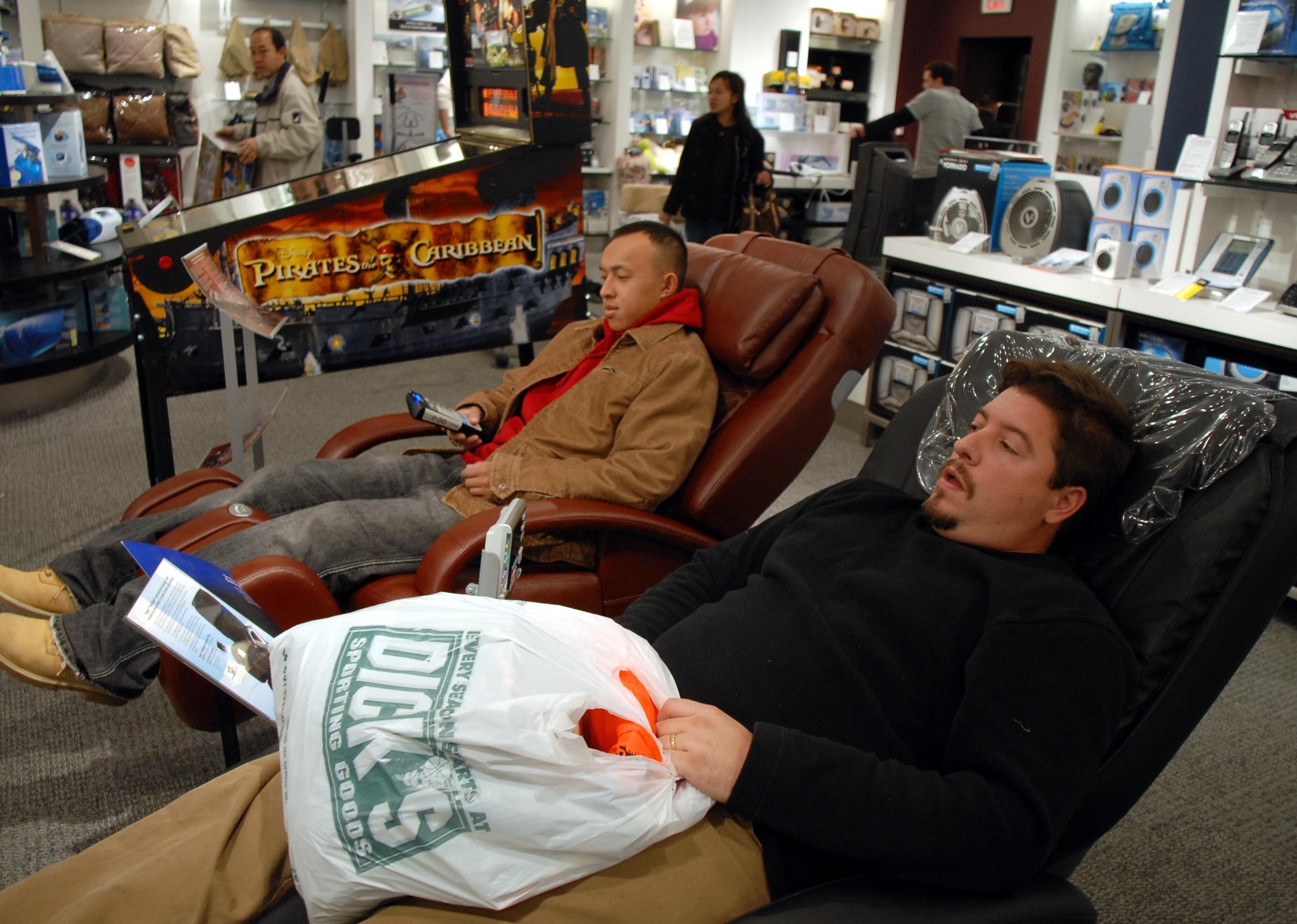Two men sitting in massage chairs at a Sharper Image store.