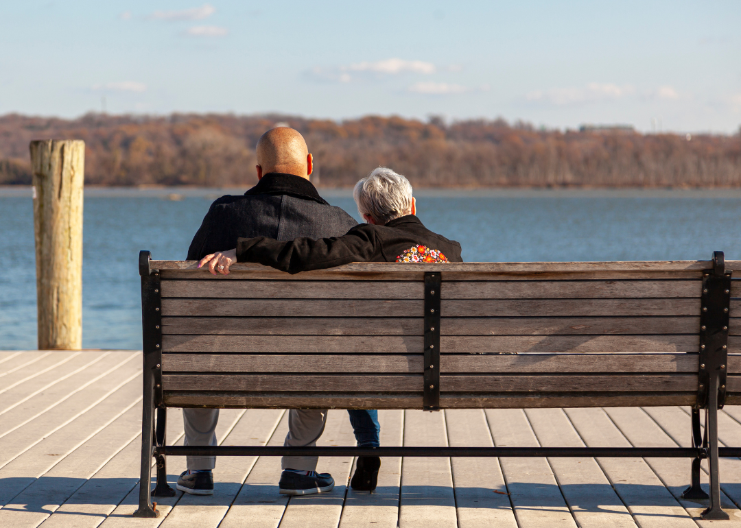 An older couple sitting on a bench looking at the water.