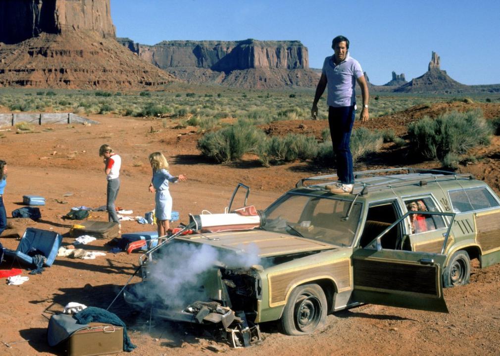 Chevy Chase stands on top of a smoking wrecked station wagon while his family stands next to the car amongst the scattered luggage.