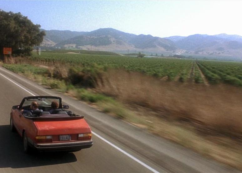 Two men in a Saab convertible drive through wine country.