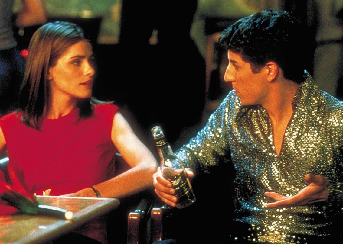 Jason Biggs, wearing a sparkly long sleeved shirt, holds a beer and talks to Amanda Peet.