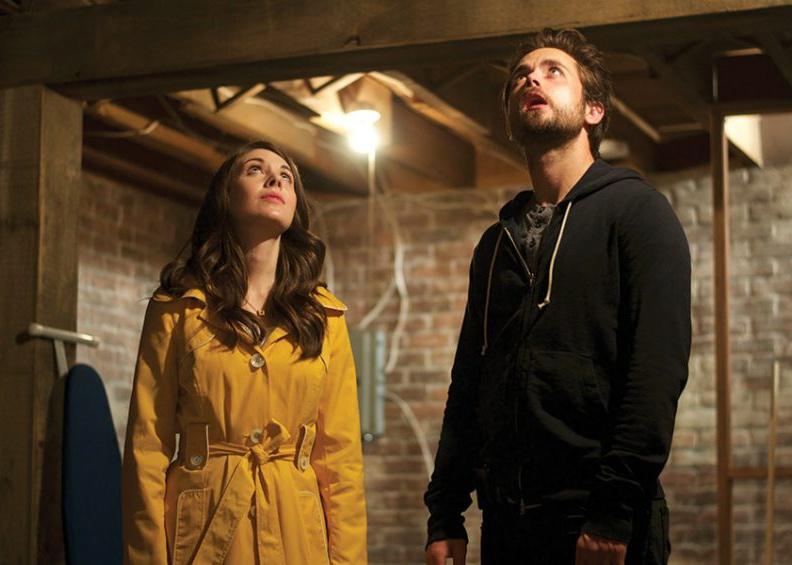 Justin Chatwin and Alison Brie in a brick basement looking up at the ceiling.
