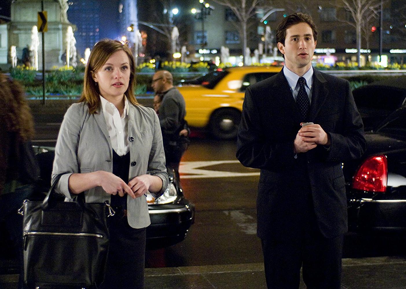 Elizabeth Moss standing near a busy street with a man in a suit.