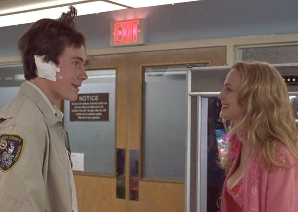 Chris Klein, in an animal control jacket with his hair sticking up, talking to Heather Graham in front of a vending machine.