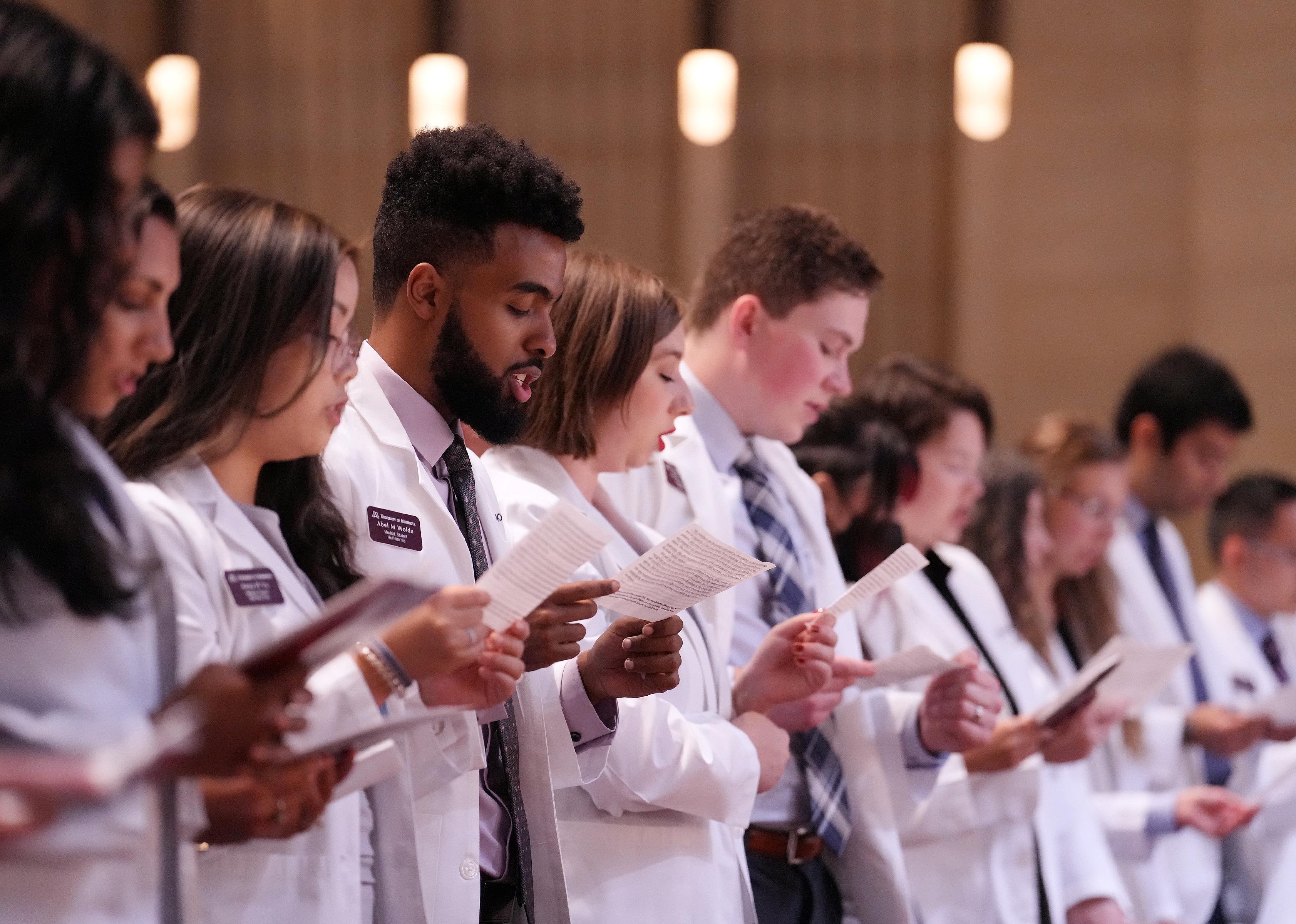 Medical students in white coats reciting a medical oath.