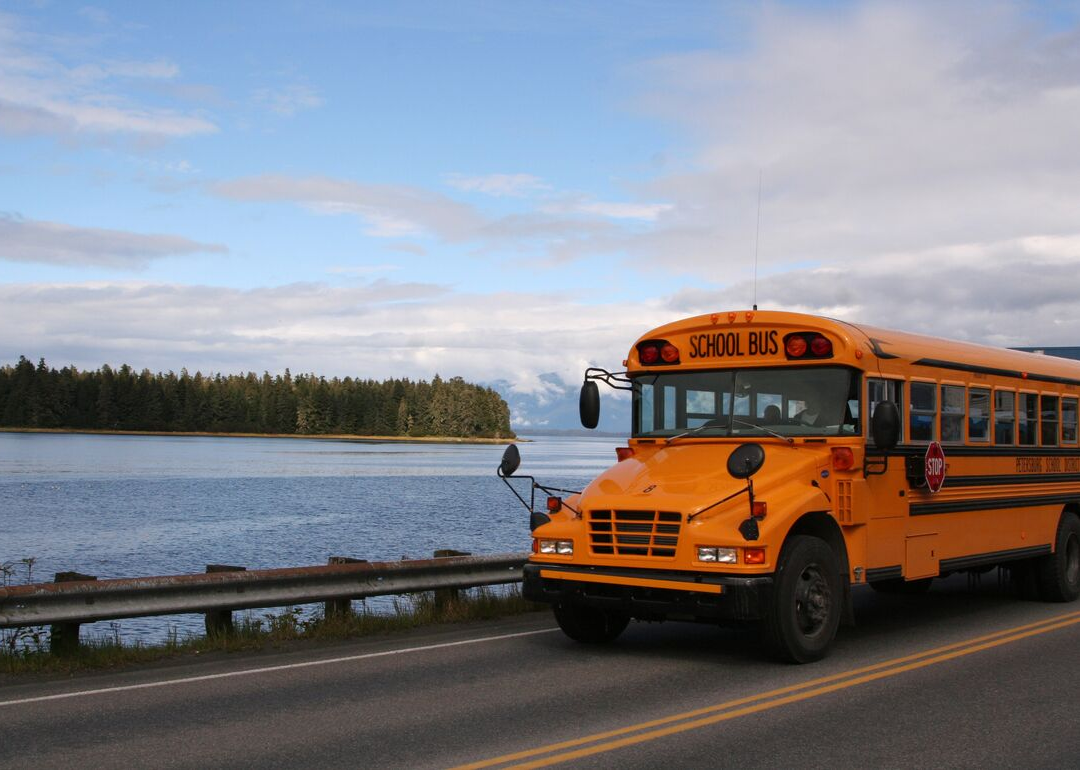 A school bus driving over a bridge with mountains in the background.