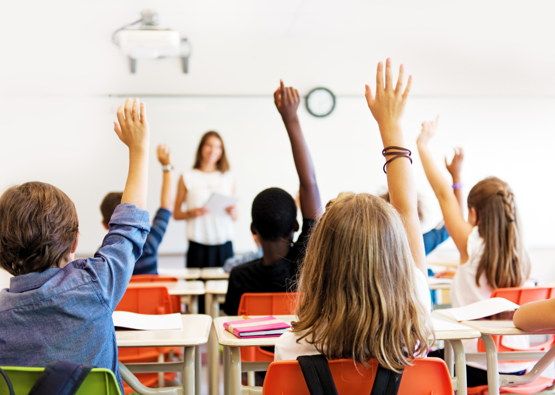 A class of school students raising their hands at their desks.