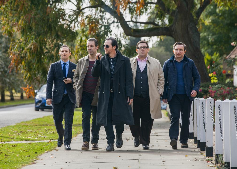 5 middle aged men in normal clothing walk down the sidewalk with a purpose.